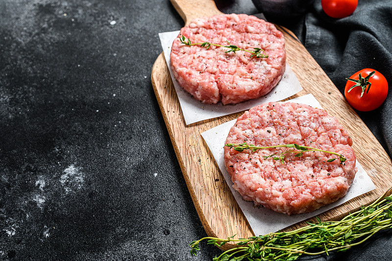 生鸡肉饼，碎肉片放在切菜板上。有机肉。黑色背景。前视图。本空间