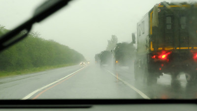 高速公路上的一列现代化军车。通过被雨覆盖的汽车挡风玻璃看到的散焦交通这是在秋天