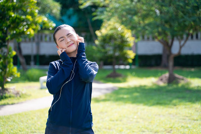 一名亚洲妇女戴着耳机在公园听音乐，皮肤痒得难受