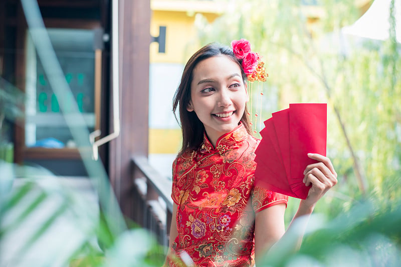 中国新年，美丽的亚洲女人穿着传统服装，拿着装有钱的红包