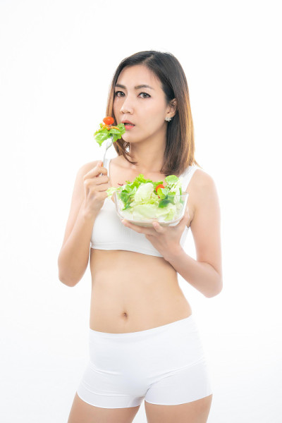 穿着白色运动胸罩的女孩拿着一个沙拉碗。