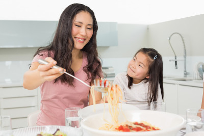 女孩看着快乐的女人在厨房端意大利面