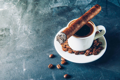 一杯咖啡，咖啡豆，烟灰缸和雪茄在黑暗的背景