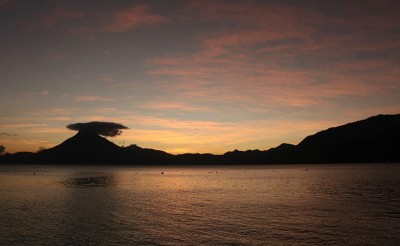 夕阳下的火山剪影与反光的水和一艘船在湖Atitlán在帕纳哈切尔，危地马拉
