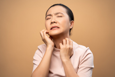 亚洲妇女是刺激物瘙痒她的皮肤孤立站在米色背景。