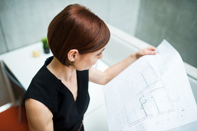 年轻的女商人或建筑师拿着蓝图站在办公室里。