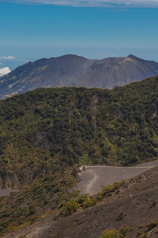 伊拉苏火山国家公园，主火山口和背景图里阿尔巴火山在一个晴朗的日子，蓝天和绿色的树叶