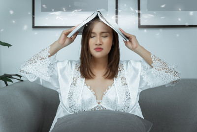 一个穿着睡衣的女人把她的书举在头上，因为读厌了课本。
