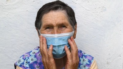 一位老年妇女用一次性面膜擦拭额头和近处有深皱纹的老脸