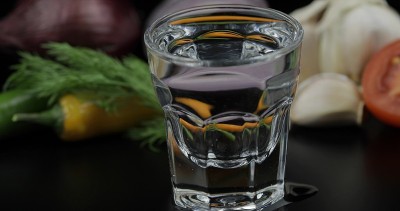 用小酒杯喝伏特加。背景用蔬菜