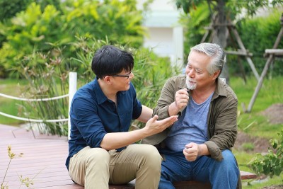 一个快乐的亚洲老人坐在河边的码头上，把他的生活经验传授给他的儿子
