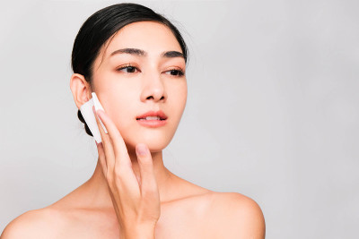 年轻美丽的亚洲女人与干净和明亮的皮肤，化妆品美丽的概念，手触摸脸颊，微笑和友好的脸孤立在灰色的背景