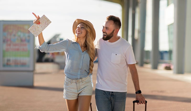 Young couple walking out airport with baggage, cop