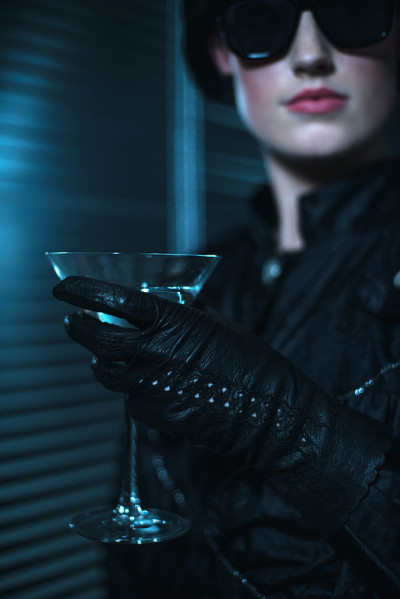 复古八十年代的女人戴着黑墨镜穿着礼服拿着鸡尾酒杯。
