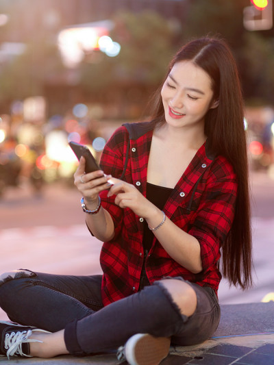 迷人的女性坐在和手握手机在模糊的步行街在晚上