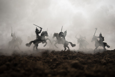 有骑兵和步兵的中世纪战斗场景。剪影的人物作为单独的对象，战斗之间的战士在日落雾蒙蒙的背景。有选择性的