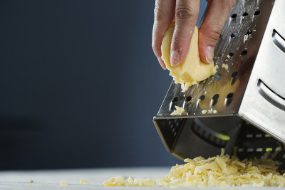 rubbing cheese on a large grater, on a wooden tabl