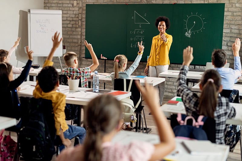 快乐的黑人老师指着在课堂上举手回答问题的小学生。