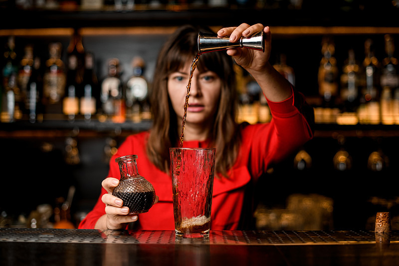 酒杯立在吧台上，女调酒师将饮料从酒桶中准确地倒入其中