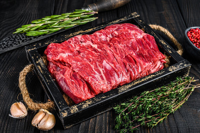 生的新鲜牛胸肉和香草在木托盘。黑色木制背景。俯视图