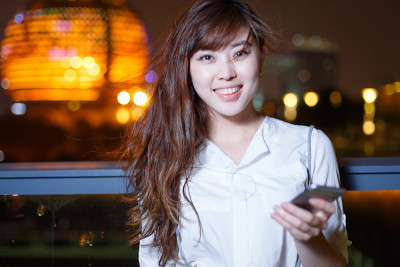 美丽的亚洲女孩在晚上使用手机