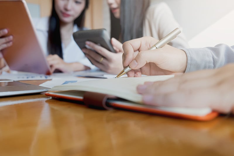 商务会议中，商务女性用笔记本电脑、计算器、股票行情表向团队领导和企业主解释分析公司的销售计划。