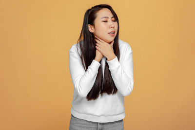 喉咙疼。不健康的年轻亚洲女孩触摸脖子遭受扁桃体炎，失去声音在黄色工作室背景