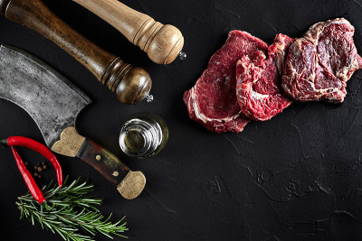 牛里脊片，用斧头切肉，用香料——迷迭香、胡椒煮在旧黑桌上。俯视图拷贝空间