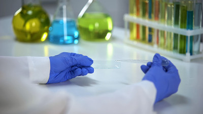 科学家拿着装有液滴的测试玻璃，洗涤剂研发实验室