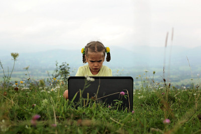 Pupil sitting on green grass outdoor and using lap
