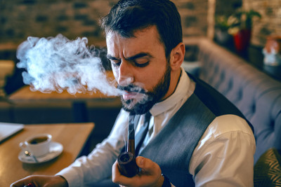 留着胡子的白人商人穿着西装坐在咖啡馆里抽着烟斗。
