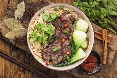 木桌上的碗里放着麻辣的红汤牛肉面