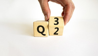 从第二季到第三季的符号。商人转动一个木方块，把单词“Q2”改成了“Q3”。美丽的白色桌子，白色的背景