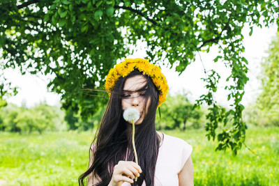 夏日模特女孩与吹长头发和花。快乐的夏天美丽的女人与健康和美丽的棕色发型与绿色的草和树叶在阳光的背景