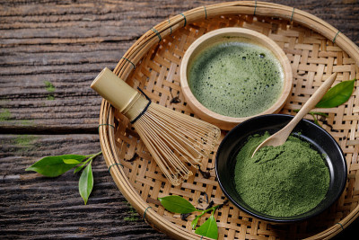日本有机抹茶绿茶粉在碗里，用铁丝打蛋器和木制背景的绿茶叶，来自大自然的有机健康产品，具有传统的风格