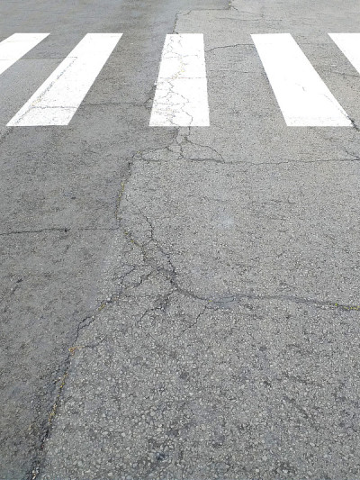 行人穿过开裂的沥青路面。地面上的白线作为背景。公路上的斑马线。人行道。
