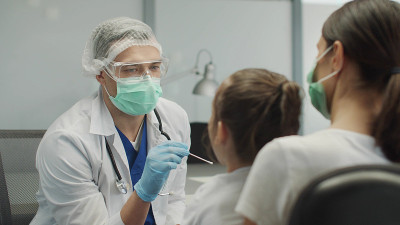 一名年轻的男性实验室助理在一名小女孩的母亲的支持下，从她的鼻咽部取样分析covid-19