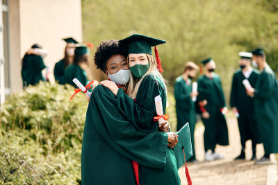 快乐的女学生们戴着防护口罩拥抱在他们的毕业日。