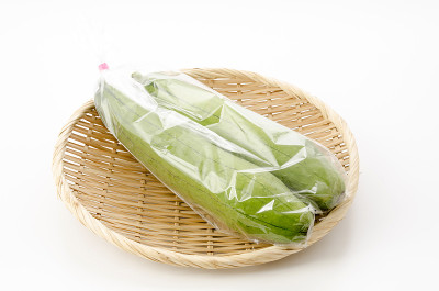 新鲜的绿色丝瓜或丝瓜放在塑料袋里，竹筛放在白色的背景上