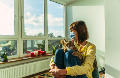 医学的面具。一个女人戴着医用口罩，怀里抱着一只猫。