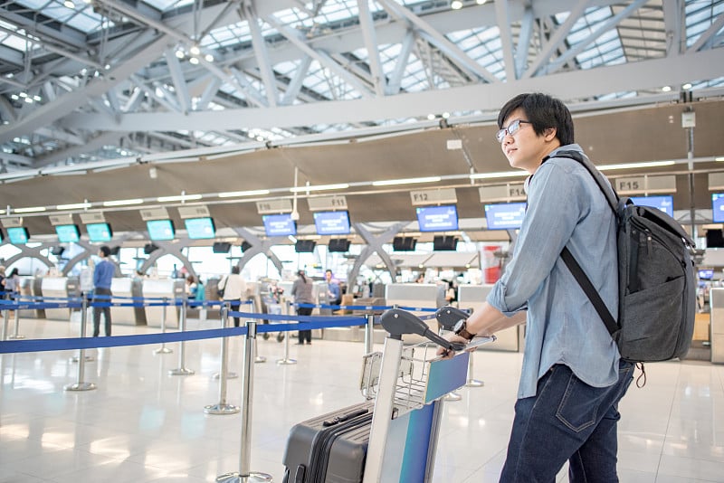 年轻的亚洲人在国际机场候机楼的航空公司值机柜台等待办理登机手续并放下行李