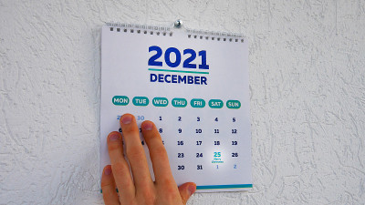 2021年墙上日历12月页的特写，有一个值得注意的圣诞节日期，旁边有一个男人的手