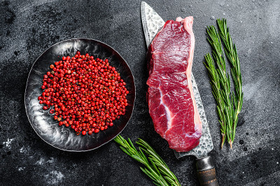 新鲜的、生的、有大理石花纹的牛腰肉，放在刀上。黑色背景。俯视图