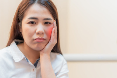 亚洲年轻女子用手触摸她的脸颊，因为有强烈的牙痛和痛苦