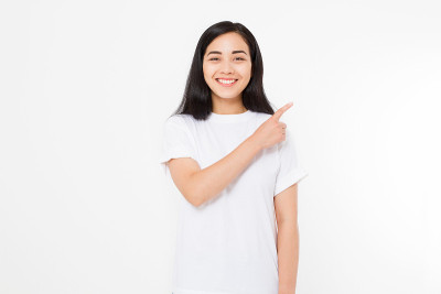 微笑的年轻亚洲女人的肖像穿着夏季t恤指着拷贝空间由手指孤立在白色模板和空白背景。