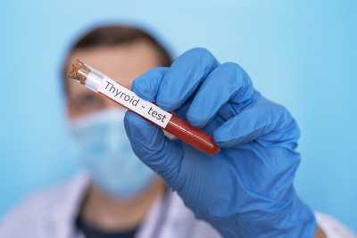 甲状腺检查医生的手拿着一个试管血液的测试在医用手套在一个蓝色的背景。
