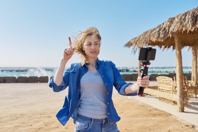 中年美丽的女人在智能手机上录制视频，日落海滩的背景