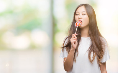 年轻的亚洲女人吃棒棒糖在孤立的背景与自信的表情在聪明的脸思考严肃