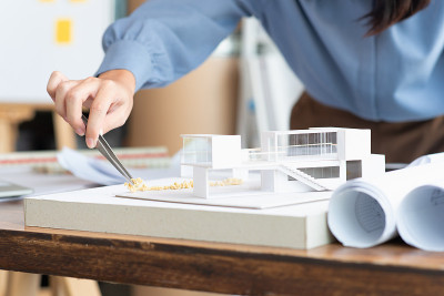 在建筑工作室中，建筑师女性用镊子在现代家庭模型上制作一个模拟灌木，建筑设计师或建筑师学生概念