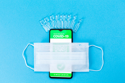 智能手机屏幕上印有COVID-19疫苗接种印章的电子免疫护照，蓝色背景上有疫苗和防护口罩。平躺